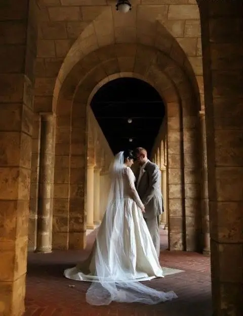 Bride and groom share tender embrace in a historic buildings stone archway on their wedding day.