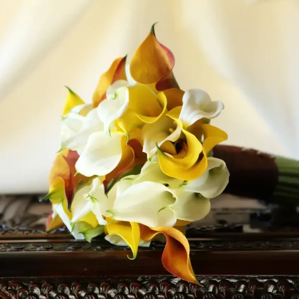 Elegant bridal bouquet with calla lilies and orchids on carved antique table.